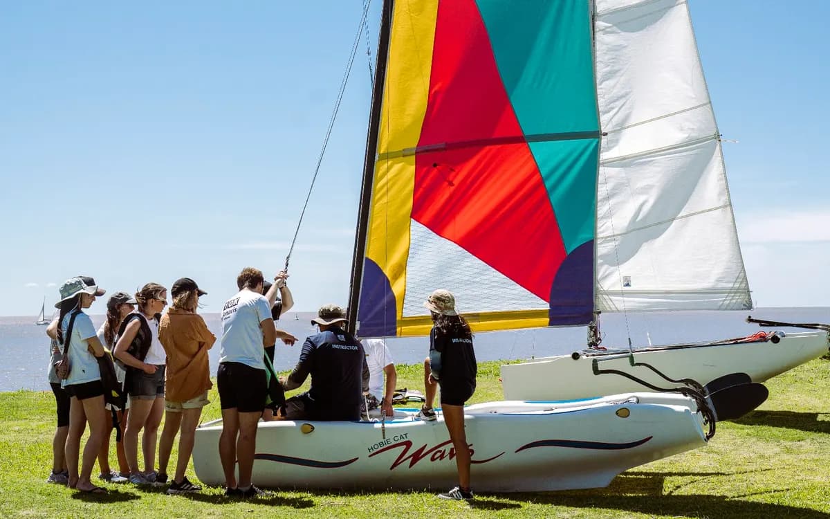 Un grupo escucha la explicación junto a un catamarán armado en la orilla