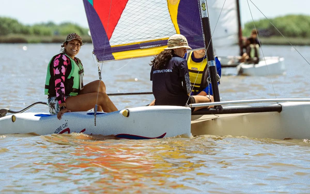 Un catamarán de velas de colores con su tripulación, cerca de la costa