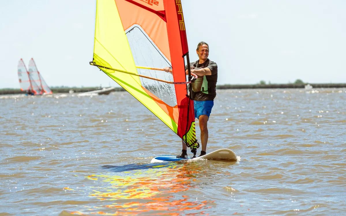 Una alumna parada en la tabla de windsurf sostiene una vela naranja