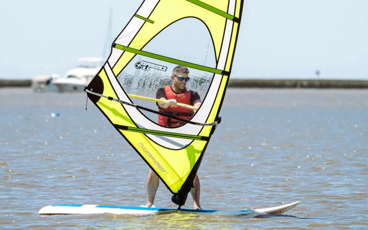 Un windsurfista navega con una vela amarilla de ventana transparente